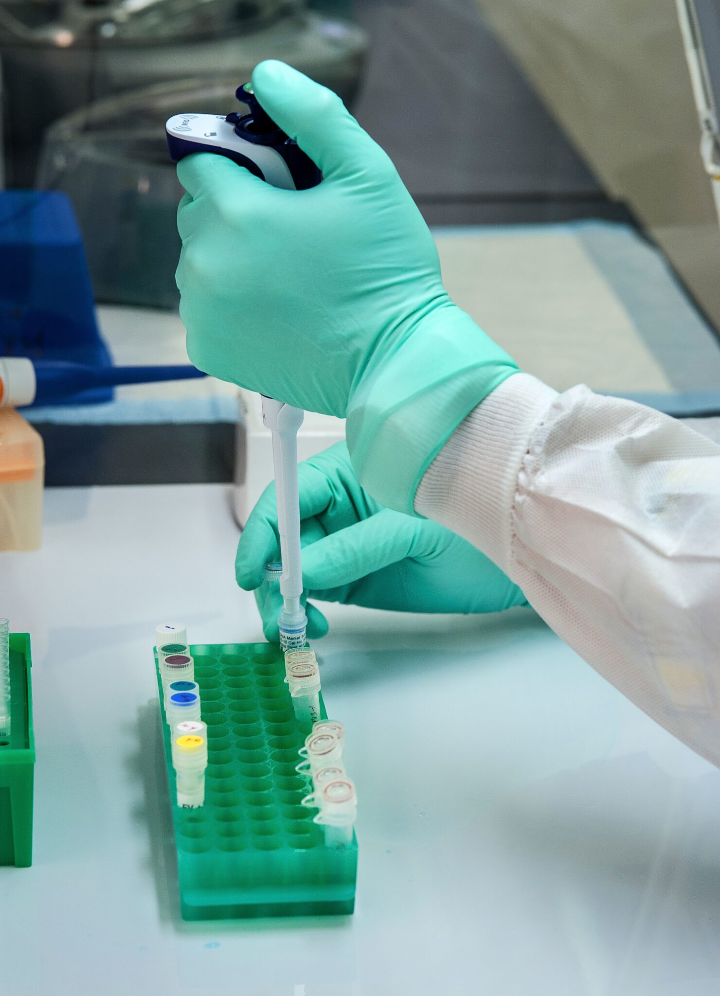 A person in gloves and green gloves is holding a test tube.